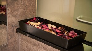Una bandeja negra con flores y hojas secas sobre una estantería frente a una pared de mármol.