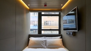 Una habitación de hotel moderna con una cama, un televisor montado en la pared y una ventana con vistas a edificios.