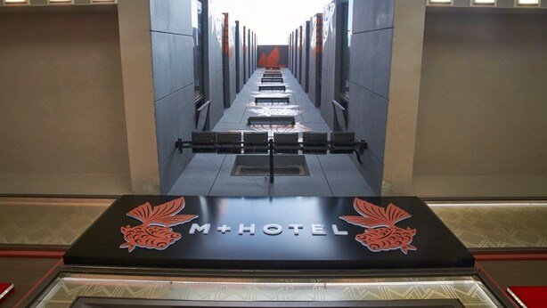 Un pasillo de hotel con un pasillo central, bancos y una recepción con un logotipo.