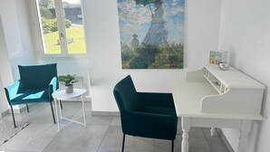 A room with a white piano, teal chairs, a small table with a plant, and a painting of a woman with an umbrella.