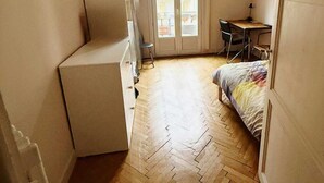 A compact room with a bed, a desk, and a chair. There is a window with curtains and a door leading to an outdoor balcony. - Nice center 4-room apartment with air conditioning (Nice)