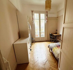 A compact room with a bed, a desk, and a chair. There is a window with curtains and a door leading to an outdoor balcony. - Nice center 4-room apartment with air conditioning (Nice)