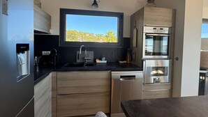 A compact kitchen with a built-in water dispenser, a window above the sink, and a stainless steel oven. - Villa Big view (Roquebrune-sur-Argens)