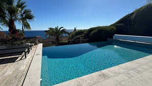 A clear blue pool with a wooden deck, palm trees, and a view of the sea. - Villa Big view (Roquebrune-sur-Argens)