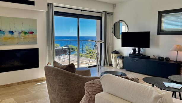 A modern living room with a large TV, comfortable seating, a balcony with a view of the sea, and a painting on the wall. - Villa Big view (Roquebrune-sur-Argens)