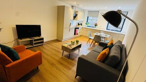 A modern living room with a flat-screen TV, orange sofa, grey sofa, and a dining area with a table and chairs. - Well-Located 2-Bed Flat, Swindon Old Town (Swindon)