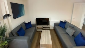 Ein modernes Wohnzimmer mit zwei grauen Sofas, einem Couchtisch, einem Flachbildfernseher und einem Gemälde an der Wand.