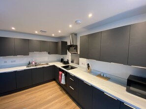 A modern kitchen with dark cabinetry, a white countertop, and a built-in stove. - 3-Bed Apartment, Swindon Old Town (Swindon)