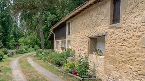 A rustic stone building with a dirt path leading to it, surrounded by lush greenery and potted plants. - Nice home in Noaillan (Noaillan)