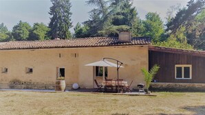 A rustic building with a tiled roof, a patio with a table and chairs, and a small garden area. - Nice home in Noaillan (Noaillan)