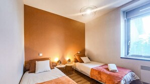 Een hotelkamer met twee bedden, een klein tafeltje, een lamp en een raam met uitzicht.