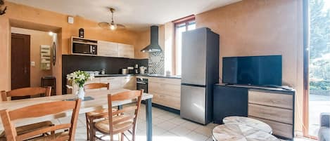 A modern kitchen with a dining area, a large refrigerator, and a flat-screen TV.