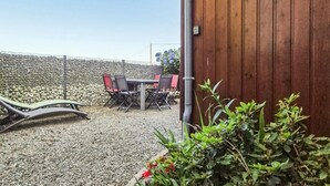 Een terras met een tafel en stoelen, een stenen muur op de achtergrond en een houten hek.
