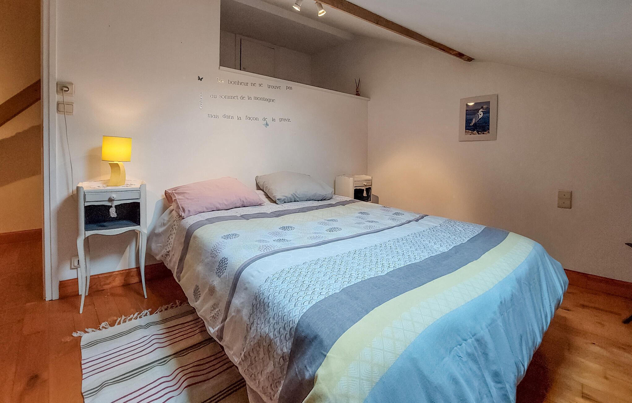 Een slaapkamer met een bed, nachtkastjes, een lamp, een vloerkleed en een aan de muur hangend schilderij.