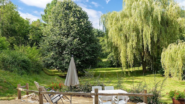 Un jardin avec une terrasse en bois, du mobilier d’extérieur et un grand arbre.