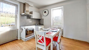 Une cuisine moderne dotée d’un four encastré et d’un coin repas avec des chaises blanches et des coussins rouges.