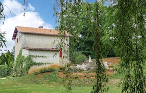 A two-story house with a tiled roof, surrounded by a garden with various plants and flowers.