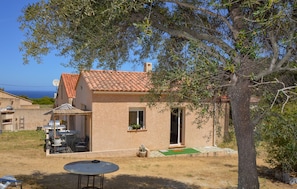 A house with a tiled roof, a patio with a table and chairs, and a small garden area.