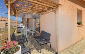 An outdoor patio with a table and chairs, a grill, and a pergola with hanging lights.