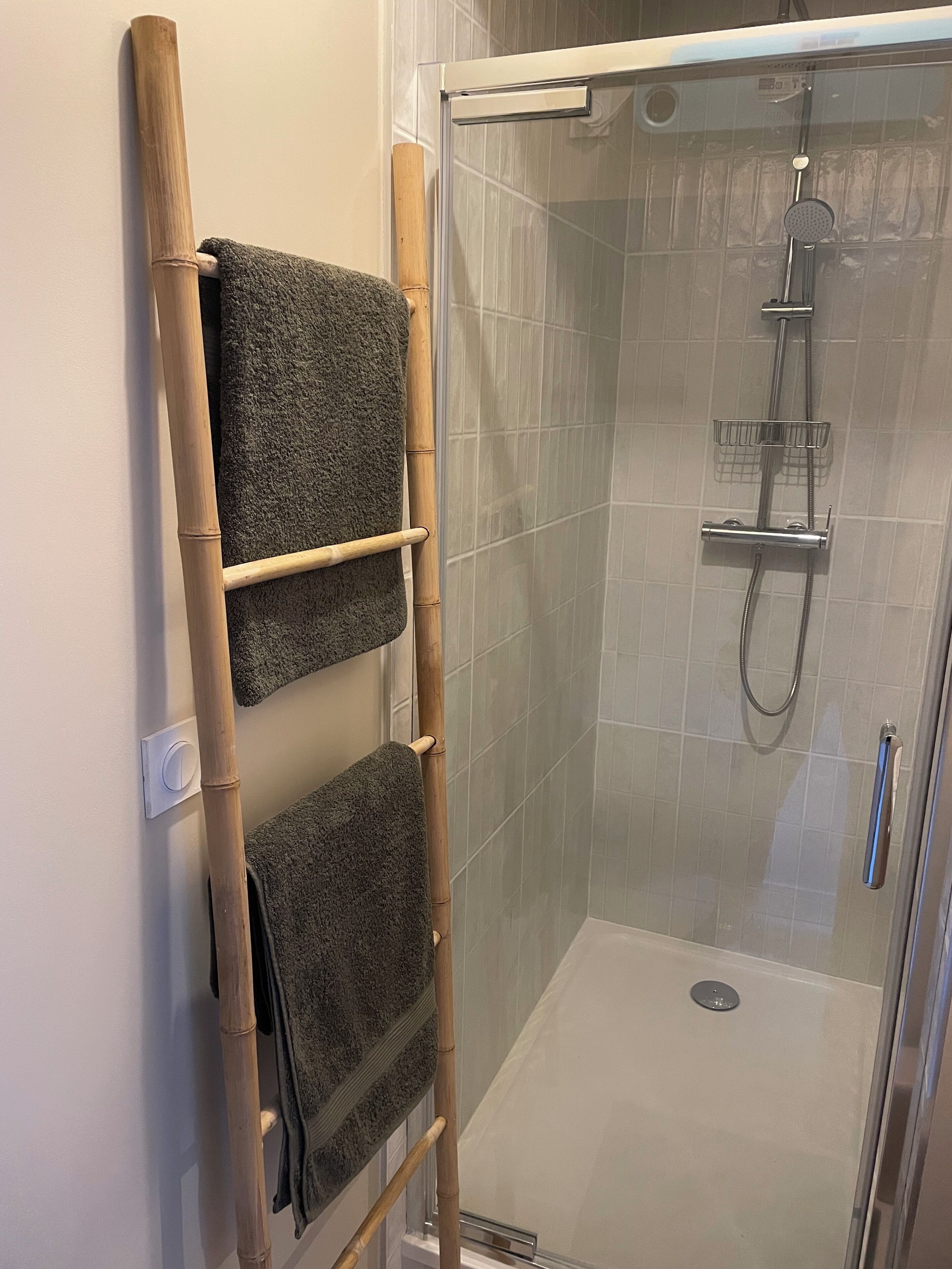 A shower area with a glass door, a bamboo towel rack with two towels, and a showerhead.
