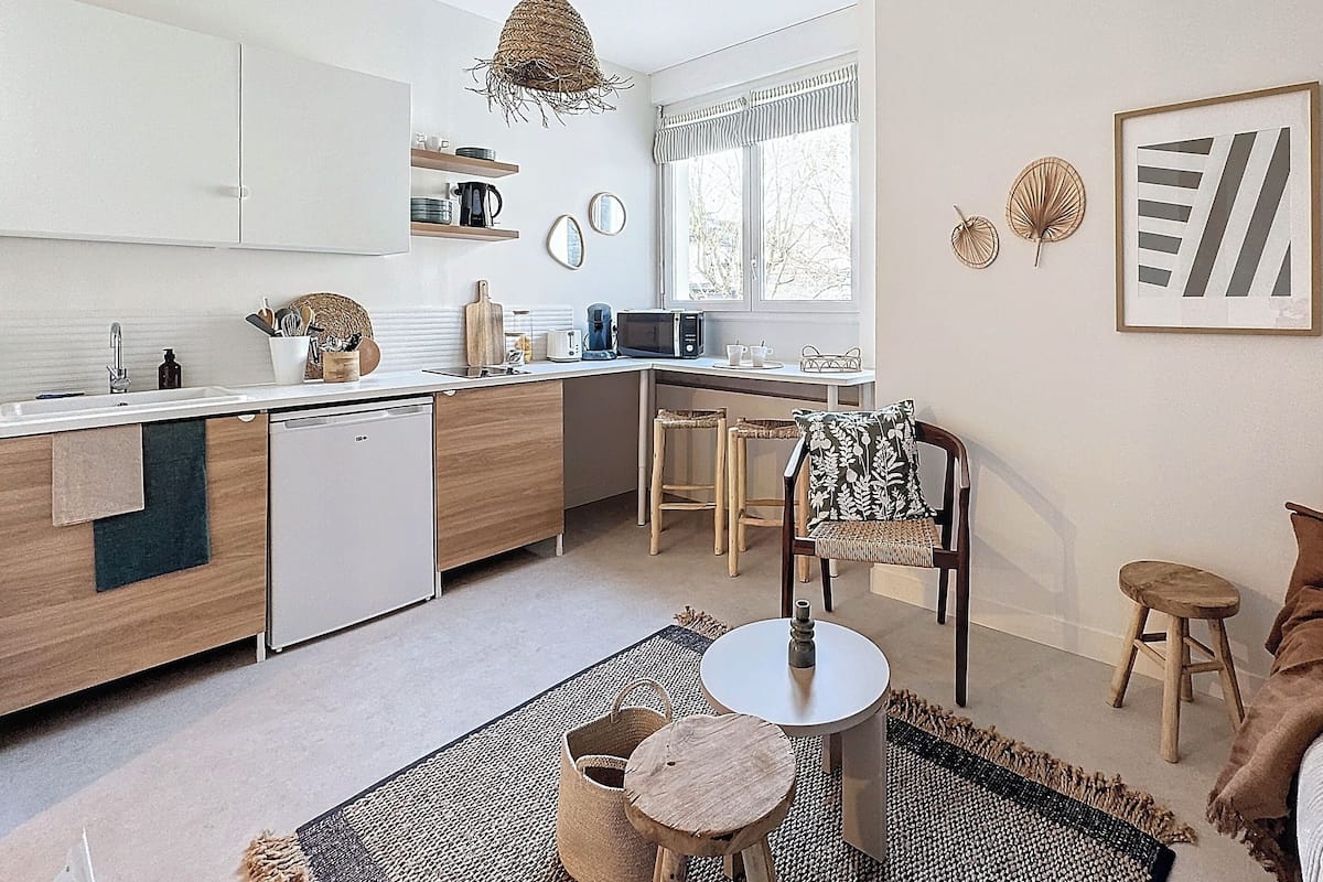 A modern kitchen with white cabinets, a built-in dishwasher, and a dining area with a wooden table and chairs.
