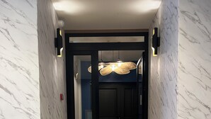 A staircase with marble walls and wooden steps leading to a room with a door and a hanging light fixture. - SacresappartsLib (Reims)