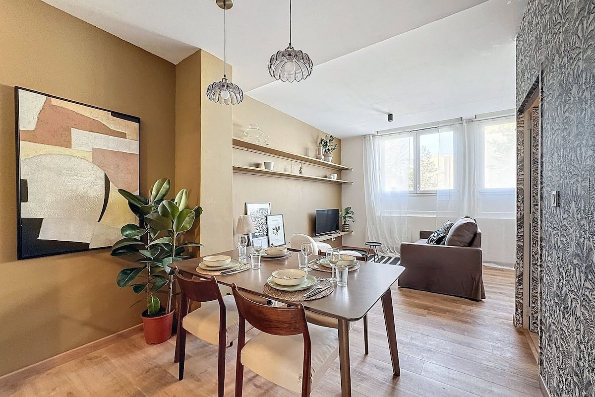 A dining area with a wooden table set for four, surrounded by chairs. There are hanging crystal pendant lights above the table.