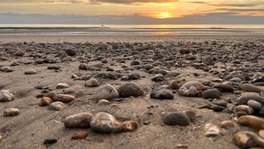 Ein Strand mit Kieselsteinen und einem Sonnenuntergang im Hintergrund.
