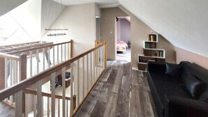 Ein geräumiges Loft mit einer Holztreppe, einem schwarzen Ledersofa und einem Bücherregal.
