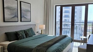 A hotel room with a large bed, two framed artworks, a nightstand with a lamp, and a balcony with a view of buildings. - Relaxed Yas Living With Resort-style Facilities (Abu Dhabi)