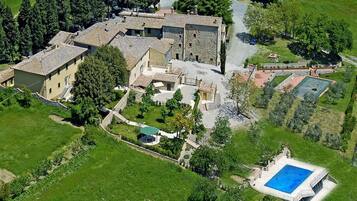 An aerial view of a property with multiple buildings, a swimming pool, and surrounding greenery.