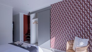 A modern bedroom with a bed, a wicker chair, and a patterned wall. - 2stay apartment Calla Bloubergstrand  (Cape Town)