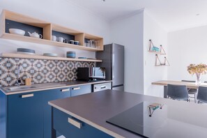 A modern kitchen with blue cabinets, a microwave, and a refrigerator. There are wooden shelves above the counter holding dishes and glasses. - 2stay apartment Calla Bloubergstrand  (Cape Town)