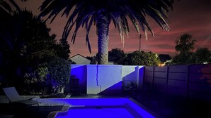 A swimming pool with blue lighting, surrounded by a fence, palm trees, and a house in the background. - 2stay apartment Calla Bloubergstrand  (Cape Town)