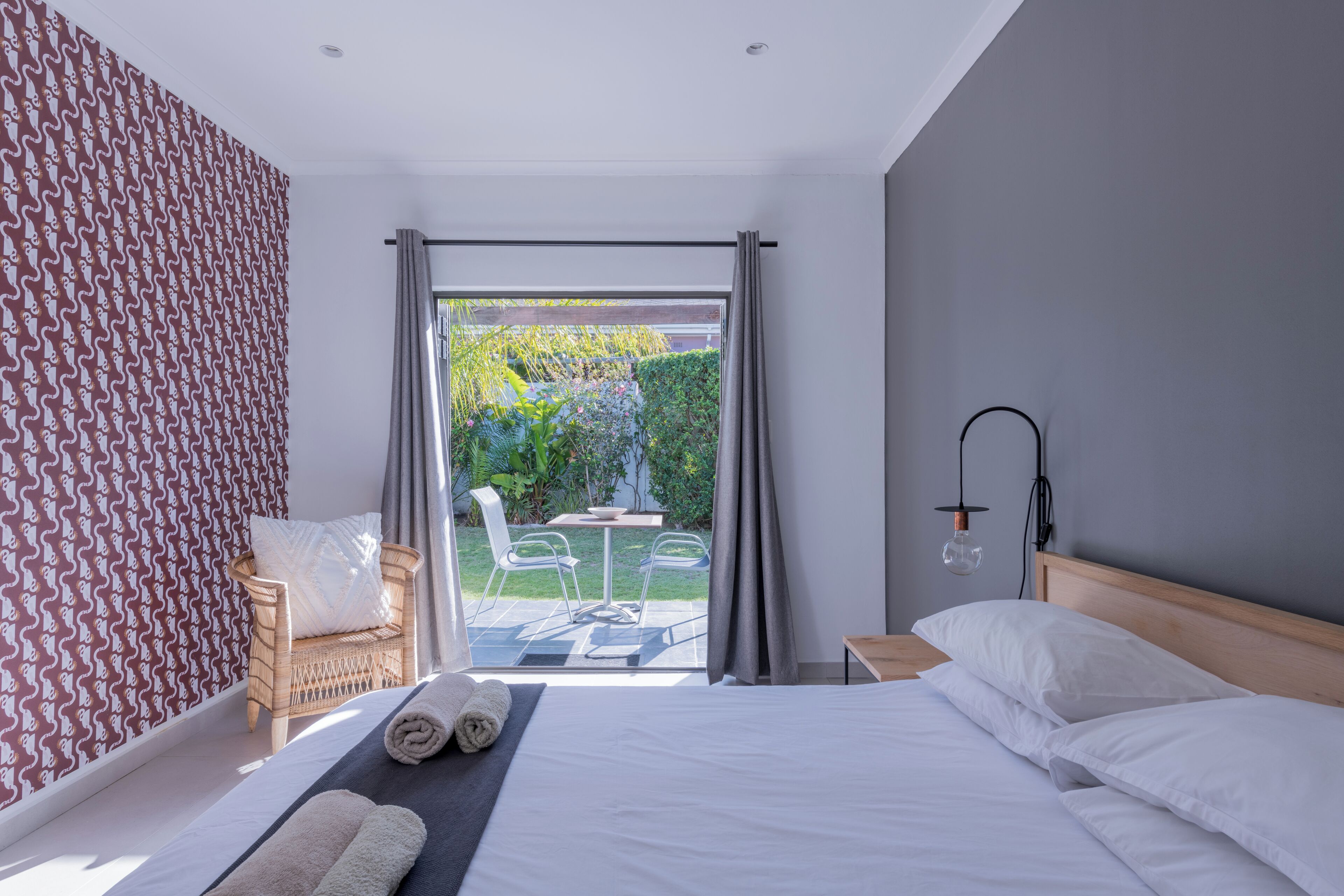 Une chambre moderne avec un lit, une chaise et une vue sur un jardin, visible à travers une porte vitrée.