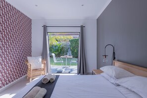 A modern bedroom with a bed, a chair, and a view of a garden through a glass door. - 2stay apartment Calla Bloubergstrand  (Cape Town)