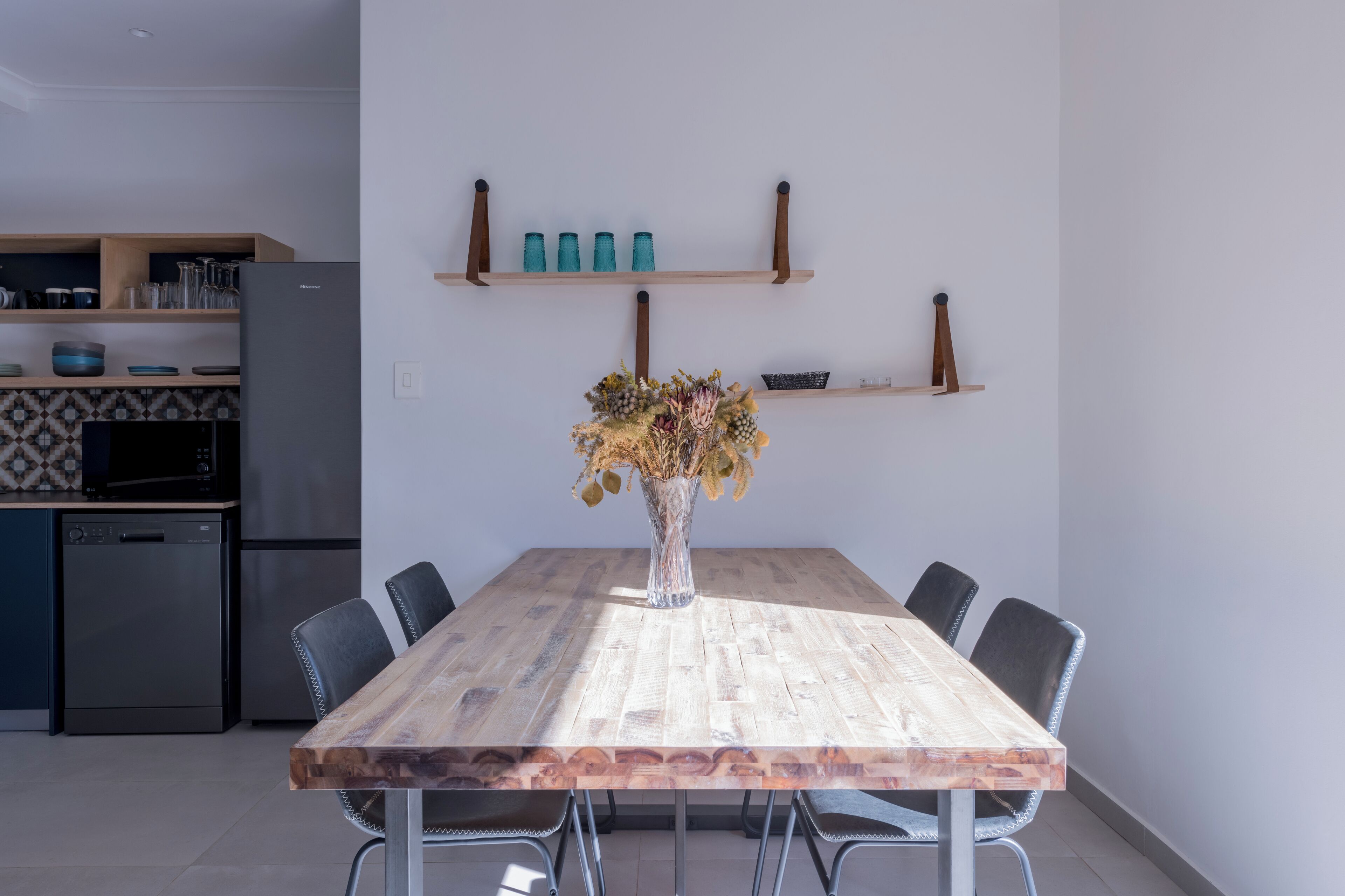 Uma cozinha moderna com uma mesa de jantar de madeira, cadeiras e um vaso de flores secas.