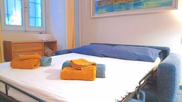 A bed with blue and orange towels, a wooden nightstand, and a painting of a landscape.
