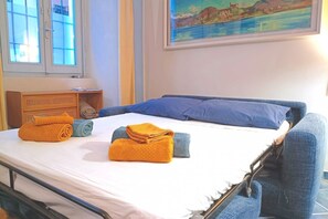 Una cama con toallas azules y anaranjadas, una mesita de noche de madera y un cuadro de un paisaje.