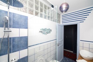 A bathroom with a shower, toilet, and sink, featuring blue and white tiles, a glass shower enclosure, and a decorative fish wall art piece.