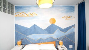 A bedroom with a bed, two bedside tables with lamps, a wall mural, and a ceiling light fixture. - Charming one-bedroom apartment, finely furnished, located on the ground floor of Via Pertossi in the historic centre of Arona.Casa Azzurra is a 52 sqm one-bedroom apartment with air conditioning, featuring a living room/kitchen area with a double sofa be (Arona)