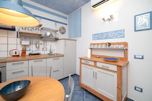Une cuisine de taille réduite avec une table en bois, un saladier bleu, une bouilloire et une machine à café.