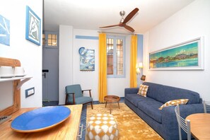 A living room with a sofa, chairs, a table, a ceiling fan, and artwork on the walls.