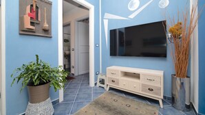 A hallway with a blue wall, a potted plant, a white console table, and a flat-screen TV mounted on the wall. - Charming one-bedroom apartment, finely furnished, located on the ground floor of Via Pertossi in the historic centre of Arona.Casa Azzurra is a 52 sqm one-bedroom apartment with air conditioning, featuring a living room/kitchen area with a double sofa be (Arona)