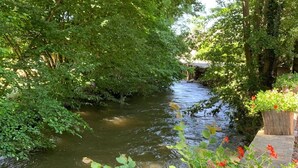 Un étroit canal bordé d’une végétation luxuriante et une structure en pierre surmontée d’un jardinière en bois.