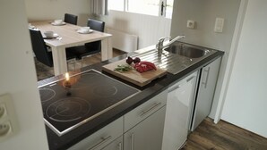 Une cuisine moderne dotée d’un plan de travail noir, d’un évier en acier inoxydable et d’une planche à découper en bois sur laquelle se trouvent des légumes.