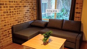 Un espace de vie avec un mur en briques, un canapé gris foncé, une table basse en bois et une fenêtre donnant sur un paysage verdoyant.