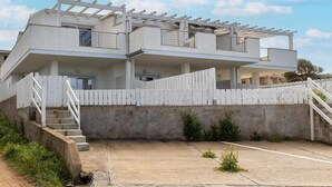 A multi-story building with a white exterior, a concrete ground floor, and a white fence. - Terrazza, air conditioning and post bus private (Paduledda)