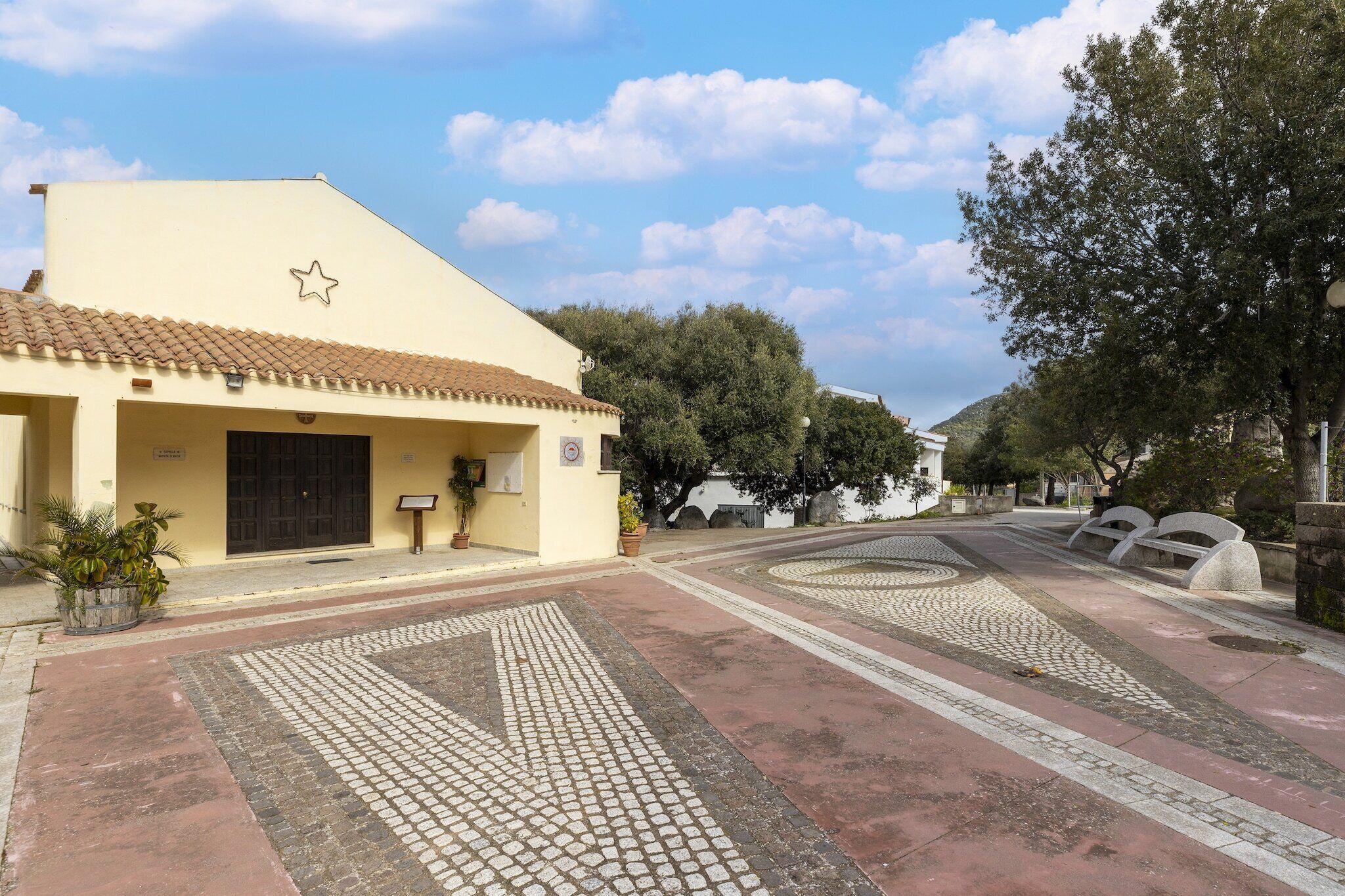 A building with a tiled roof, a star symbol, and a paved courtyard with benches.