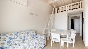 A room with a white sofa, a dining table with chairs, a staircase, and an air conditioning unit. - Terrazza, air conditioning and post bus private (Paduledda)